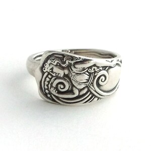 May include: A silver ring made from a repurposed spoon with an ornate design featuring a woman and a swirling pattern.