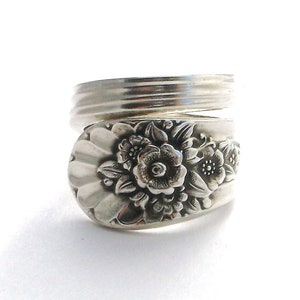 May include: A silver ring made from a vintage spoon with a floral design. The ring is wrapped around the spoon handle, creating a unique and stylish piece of jewelry.