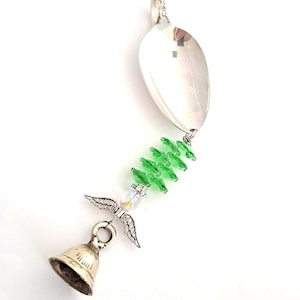 May include: A handcrafted wind chime featuring a repurposed silver spoon. Green faceted beads cascade down to a small silver bell. An angel charm with outstretched wings is attached to the bell.