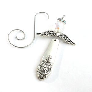 May include: A silver-toned metal ornament shaped like an angel, featuring a floral-patterned spoon handle as the body, metallic wings, and a clear iridescent bead head topped with a small rhinestone spacer, accompanied by a curved wire hook.