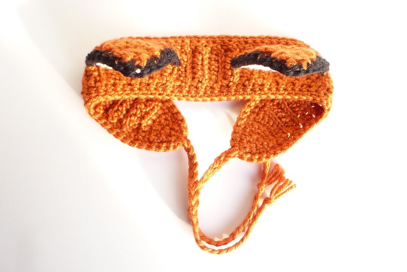 May include: Orange crocheted headband with black ears. The headband has a long tie that can be tied under the chin.