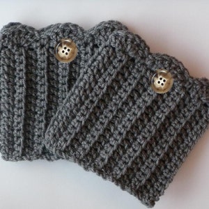 Puede incluir: Tres calentadores de piernas de crochet grises con botones. Los calentadores de piernas están hechos con un patrón de punto simple y tienen una textura acanalada.