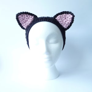 May include: A black headband with pink cat ears. The headband is made of crocheted yarn.