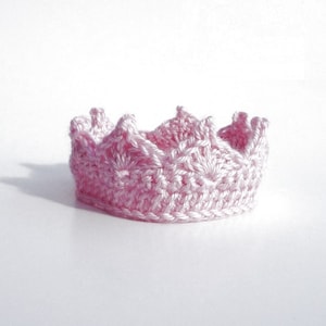 May include: A pink crocheted crown with a pointed top and scalloped edges.