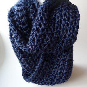 May include: A navy blue crocheted infinity scarf. The scarf is made with a chunky yarn and has a textured stitch pattern.