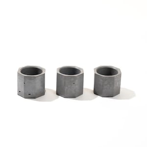 May include: Three gray concrete hexagonal planters, each with a smooth, slightly textured surface. The planters are arranged in a row on a white background.