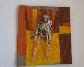 Day of the Dead Fabric art quilt with plastic skeleton with wings,fiber art,Fall colors,orange,yellow,brown,wall hanging,Mexican inspired