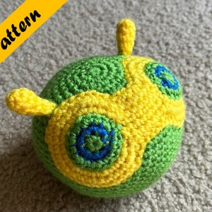 May include: A crocheted ball toy with a green, yellow and blue pattern. The ball has three yellow antennae.