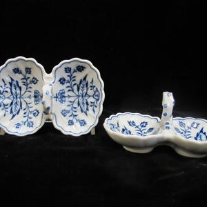 May include: Two-piece ceramic serving dishes with a blue floral pattern on a white background. One dish is butterfly-shaped, and the other has a handle. Both have scalloped edges and are likely for serving condiments or small portions.