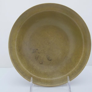 Peut inclure: Un bol circulaire peu profond avec une finition vert olive sourd. La surface intérieure présente une texture lisse et mate avec de subtiles variations de couleur et quelques petites taches sombres et irrégulières au fond du bassin.