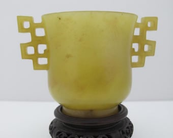 Copa de libación china arcaica de jade amarillo con dos asas y soporte de madera tallada.