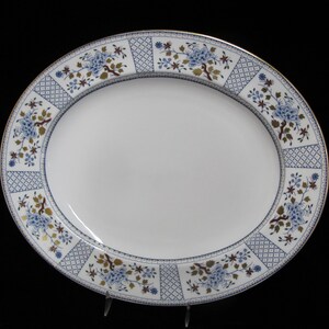 Puede incluir: Un plato ovalado blanco para servir con un patrón floral azul y dorado alrededor del borde.