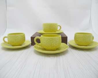 Könnte beinhalten: Ein Set aus sechs gelben Keramik-Tassen und Untertassen. Die Tassen und Untertassen haben ein strukturiertes Blumenmuster. Die Tassen haben Henkel und stehen auf einer weißen Holzoberfläche.