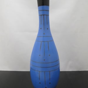 Puede incluir: Un jarrón de cerámica azul con la parte superior negra. El jarrón tiene una forma delgada y alargada con líneas y puntos negros decorativos. El jarrón mide aproximadamente 25 cm de alto.