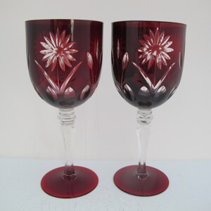 May include: Two red wine glasses with etched white floral designs. The glasses have clear stems and bases.