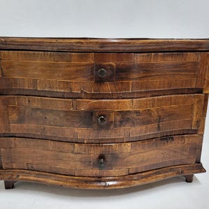 May include: A small, three-drawer wooden chest with a curved front and dark brown wood finish. The drawers have simple metal pulls.