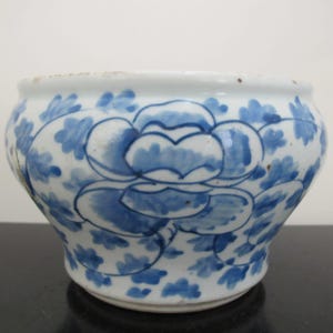 Op de afbeelding: Een witte keramische kom met een blauw en wit bloemenmotief. De kom heeft een ronde vorm en een brede rand.