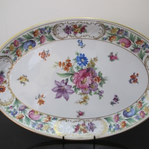 May include: A white oval serving platter with a gold rim and floral design. The platter features a central bouquet of pink, purple, blue, and yellow flowers with green leaves. The border is decorated with smaller floral motifs in shades of pink, blue, yellow, and green.