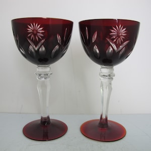 May include: Two red wine glasses with clear stems and bases. The glasses have a cut glass design with a floral pattern.