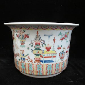 Puede incluir: Una maceta de cerámica blanca con borde acampanado, adornada con escenas pintadas a mano de flores, pájaros y elementos arquitectónicos coloridos. La maceta presenta un borde decorativo con patrones geométricos y florales.