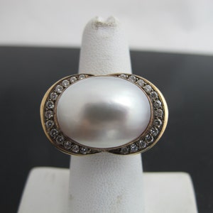 May include: A gold ring with a large white pearl set in a halo of small clear stones.