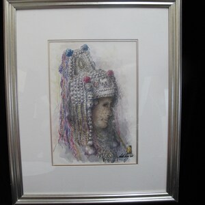 May include: Watercolor portrait of a person wearing a detailed, ornate headdress with colorful accents. The artwork, framed in silver, depicts a side profile with a pipe. The style is reminiscent of traditional portraiture.