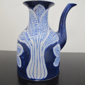 May include: A blue and white ceramic pitcher with a long spout and a wide base. The pitcher is decorated with a tree-like pattern in white against a blue background. The rim is white with a blue border.