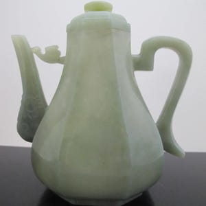 May include: A pale green jade teapot with a lid and a handle. The teapot has a rounded body and a hexagonal base.