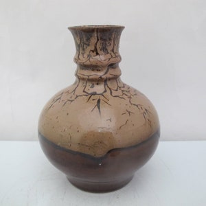 Può includere: Un vaso in ceramica marrone con una base larga e un collo stretto. Il vaso ha una smaltatura marrone chiaro con linee di craquelé marrone scuro.
