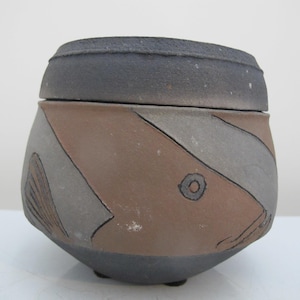May include: A ceramic pot with a lid, featuring a geometric pattern in shades of brown, gray, and white. The pot has a rounded shape and a slightly flared rim.