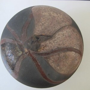 May include: A round ceramic bowl with a dark gray glaze and a brown design. The design features a stylized flower with five petals.