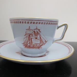 Peut inclure: Une tasse à thé et une soucoupe blanches avec un motif de bateau rouge et blanc. La tasse a une bordure dorée et une anse. La soucoupe a une bordure rouge et blanche.