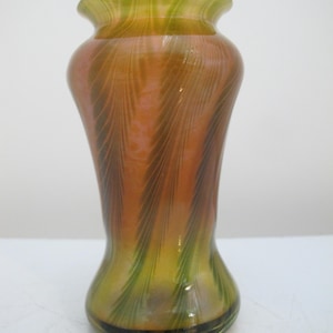 Può includere: Un vaso decorativo in vetro con bordo svasato e base bulbosa. Il vaso presenta una miscela di colori, tra cui arancione, verde e marrone, con un motivo a spirale. Il vaso è alto circa 20 cm.