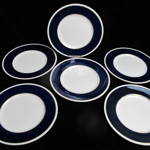 Pode incluir: Conjunto de seis pratos rasos brancos com borda azul marinho e um detalhe dourado. Os pratos têm uma borda perolada.