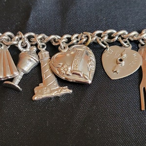 May include: A silver charm bracelet with various charms, including a lighthouse, a heart with the word "Forever" inscribed on it, a compass, a fork and spoon, and a seashell.