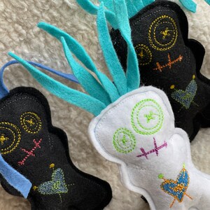 May include: Three handmade felt toys with embroidered faces and hearts. The toys are black, white, and blue with colorful stitching.