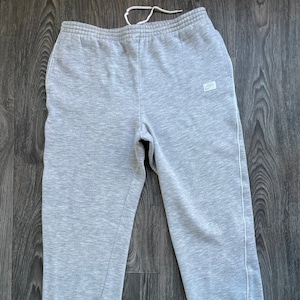 Könnte beinhalten: Graue Jogginghose mit weißen Paspeln an den Seiten und einem kleinen weißen Nike-Logo-Patch am linken Bein.