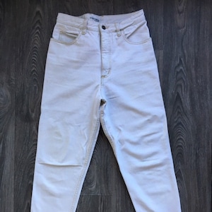 Puede incluir: Vaqueros blancos de cintura alta con un detalle de cremallera en los laterales de las piernas.