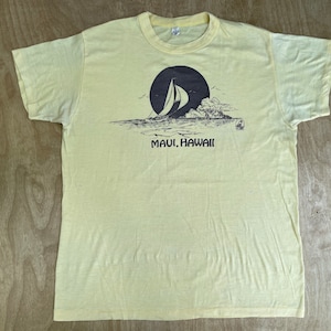 May include: A yellow t-shirt with a black and white graphic of a sailboat in front of a large island. The text "MAUI, HAWAII" is printed below the graphic.