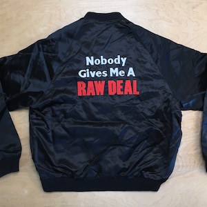 May include: Black satin bomber jacket with the text "Nobody Gives Me A RAW DEAL" embroidered on the back in white and red.