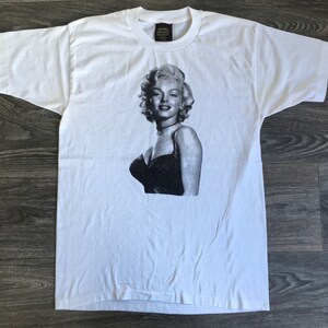 May include: White t-shirt featuring a black and white image of Marilyn Monroe in a black dress.
