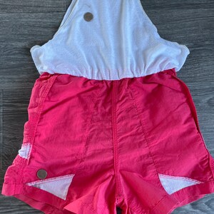 May include: A pink and white athletic jumpsuit with a white tank top and pink shorts. The shorts have white mesh panels on the sides.