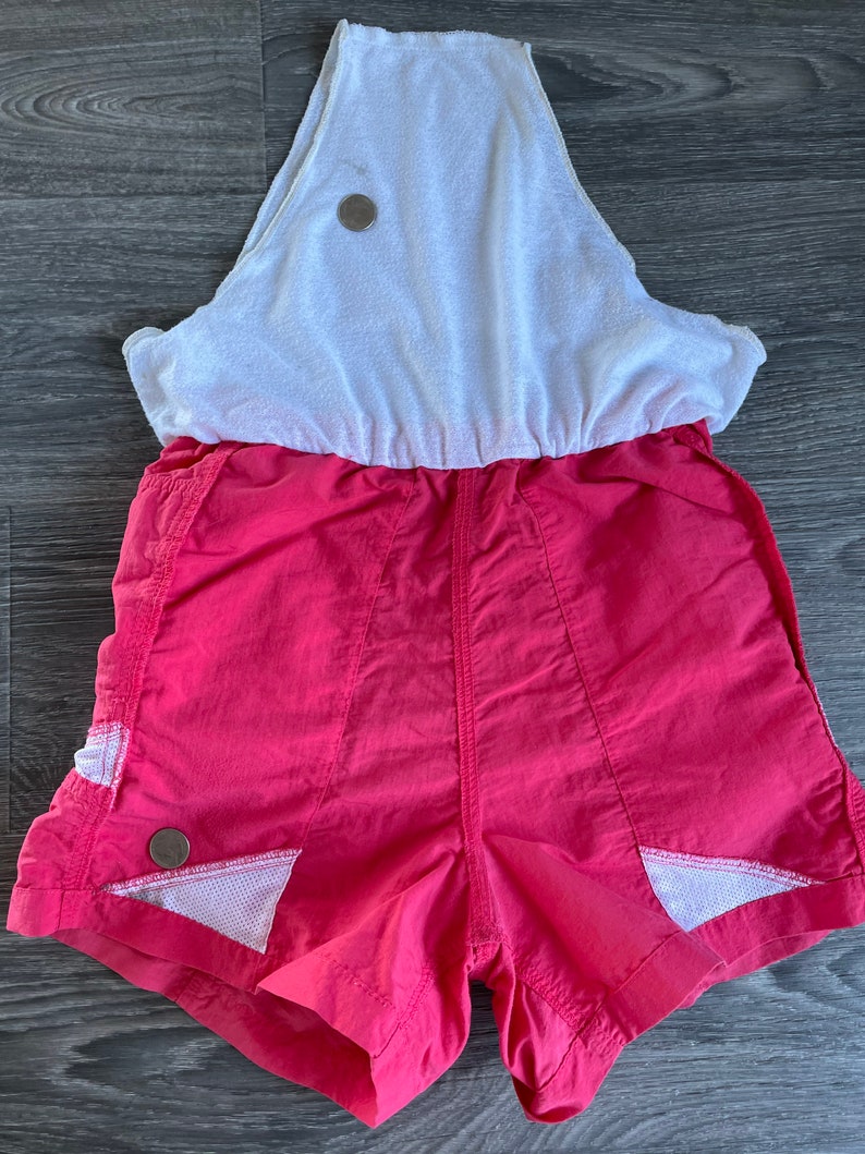 May include: A pink and white athletic jumpsuit with a white tank top and pink shorts. The shorts have white mesh panels on the sides.