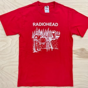 May include: Red t-shirt with a white graphic of a band, Radiohead, and a cartoon image of a truck and people.