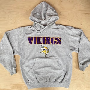 Könnte beinhalten: Grauer Kapuzenpullover mit einem lila und gelben Minnesota Vikings Logo und dem Wort "VIKINGS" in lila und gelben Buchstaben.