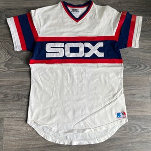 Puede incluir: Jersey de béisbol blanco con rayas azules y rojas en las mangas y una franja roja y azul a través del pecho. El jersey tiene la palabra "SOX" en letras blancas en el pecho. El jersey tiene un logotipo de la Major League Baseball en la parte inferior derecha.