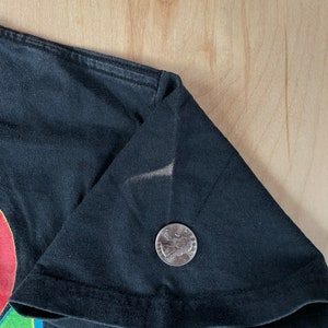 May include: Close-up of the black fabric of a t-shirt with a colourful graphic design. A US quarter is included for scale.