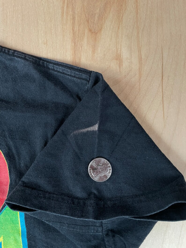 May include: Close-up of the black fabric of a t-shirt with a colourful graphic design. A US quarter is included for scale.