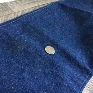 Puede incluir: Primer plano de tela vaquera azul oscuro con una textura sutil. Una moneda de plata se coloca sobre la tela para la escala.