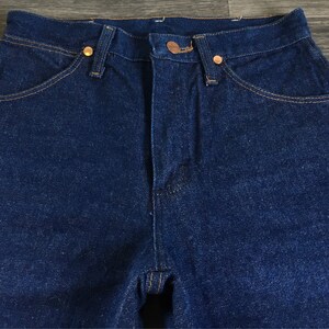 Puede incluir: Un par de pantalones vaqueros de mezclilla azul oscuro con un estilo cl&aacute;sico de cinco bolsillos. Los pantalones tienen una cintura alta y una pierna recta.